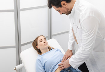 Doctor gastroenterologist palpating female patient's stomach and examining abdomen in clinic for...