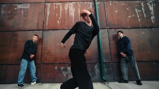 Redheaded breakdancer performing dynamic street dance moves with two crew members near contemporary urban setting, highlighting freestyle hip-hop skills