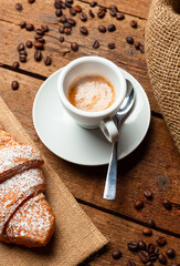 Steaming cup of espresso with croissant and coffee beans on wooden table