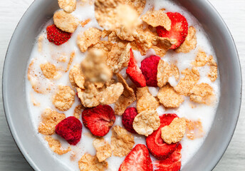 Cornflakes and freeze dried berries falling into a bowl of milk creating a healthy breakfast