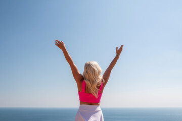 Obraz premium A woman in a pink top and white skirt is standing on a cliff overlooking the ocean. She is smiling and she is happy.