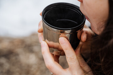 A woman is taking a sip from a stainless steel drinking cup that she holds in her hand, showcasing...