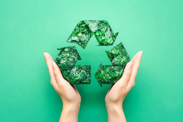 Hands holding green plastic recycle symbol on green background, promoting environmental awareness, sustainability and responsible plastic waste management. Copy space