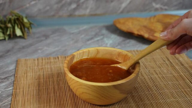 We stir the ready-made cloudberry jam with a wooden spoon in a plate. Cloudberry jam in a wooden plate. Close-up.