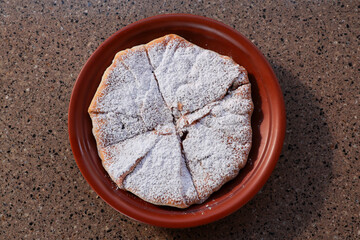 homemade Moldavian cake with cherries sprinkled with a layer of ground sugar on a brown plate