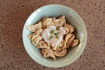 traditional dish of pelmeni with cream in a light green deep plate