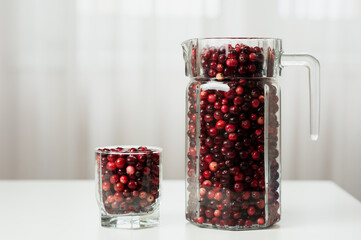 Cranberry. Small forest red berry. Cranberries in a jug and in a glass on the table. A glass of cranberries. Vitamins from nature. Selective focus.