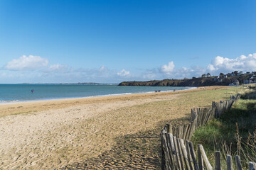 Fototapeta premium Grande Plage de Saint-Cast-le-Guildo sous un ciel bleu hivernal, étendue de sable et mer scintillante.