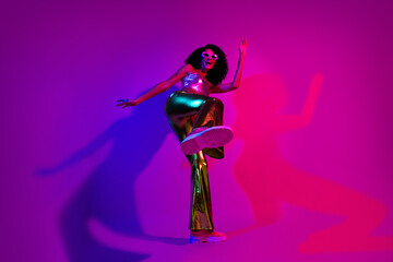 Obraz premium Young stylish woman in vibrant glowing outfit dancing under vivid neon pink and purple light with joyful energy.