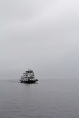 A dramatic and atmospheric photograph of a ship slowly navigating through the thick fog on Lake Como. The mist envelops the boat, creating a sense of mystery and adventure