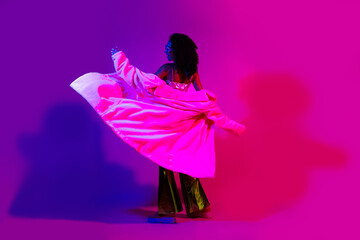 Stylish young woman in vintage fashion dancing with neon pink and purple background lighting, expressing trendy and glamorous energy