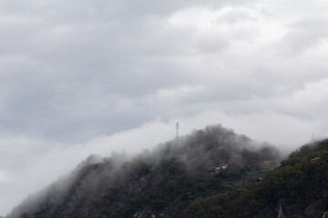 Fototapeta premium A stunning and atmospheric view of foggy mountains towering over the tranquil waters of Lake Como. The mist hangs over the mountain peaks