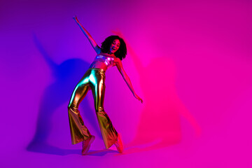 Young woman in vibrant disco outfit dancing with neon pink and purple lighting in the background