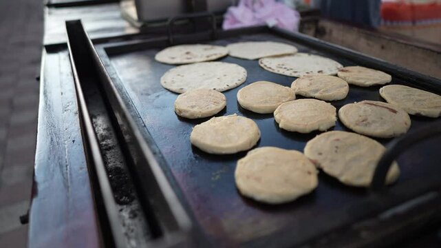 A street vendor cooks fresh pupusas and quesillo on a hot griddle in Granada, Nicaragua. Locals and tourists enjoy the vibrant market atmosphere while savoring traditional food.