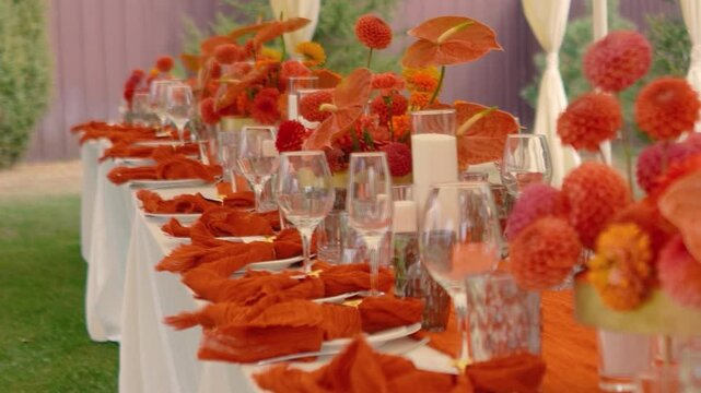 Orange autumn flowers dahlias on table with decor, floristry and food. Outdoor tent in nature. Festive buffet and many delicious dishes with glasses at banquet and celebration of wedding and event
