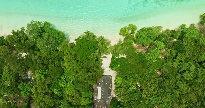 A breathtaking aerial view of a secluded Mai Ngam beach with crystal-clear turquoise waters, surrounded by lush green vegetation and corel reef. The pristine white sand and vibrant ocean hues