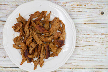 Shredded seitan, mock chicken, on white plate, wooden table. Copy space.