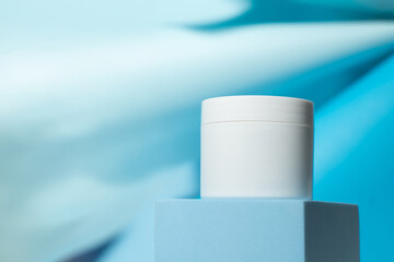 White cosmetic jar on a blue stand on a blue background. Cosmetics, science and medicine. Background for the cosmetics industry.