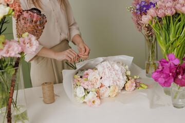 Female florist creating a delicate bouquet with fresh flowers in a floral workshop, surrounded by...