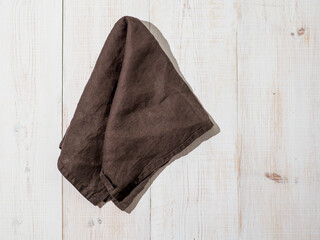 Brown linen kitchen towel or textile napkin on white wooden background.