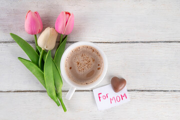 Mother’s Day breakfast background featuring croissant, strawberries, chocolates, coffee mug, bouquet of tulip flowers, as surprise and gift, with greeting card 