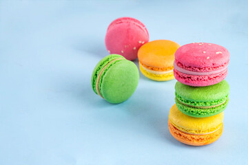 Bright and colorful sweet macaroons dessert with fresh berries. Pink, orange, yellow and pistachio green tasty macaron cookies on light blue background copy space