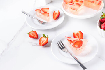 Japanese Raindrop Cake, or Mizu Shingen Mochi, clear jelly dessert, crystal-clear water-like delicacy agar pudding tart with strawberry slices, portioned on plates, white marble background copy space