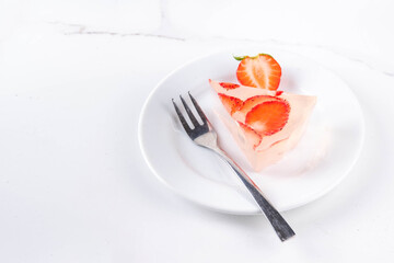 Japanese Raindrop Cake, or Mizu Shingen Mochi, clear jelly dessert, crystal-clear water-like delicacy agar pudding tart with strawberry slices, portioned on plates, white marble background copy space