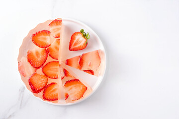 Japanese Raindrop Cake, or Mizu Shingen Mochi, clear jelly dessert, crystal-clear water-like delicacy agar pudding tart with strawberry slices, portioned on plates, white marble background copy space