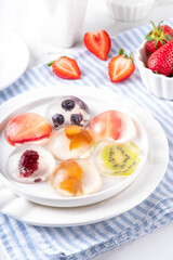 Japanese Raindrop Cake, or Mizu Shingen Mochi, clear jelly dessert, crystal-clear water-like delicacy agar pudding with fruit and berry slices, portioned on plates, white marble background copy space
