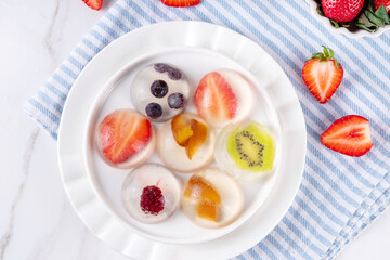 Japanese Raindrop Cake, or Mizu Shingen Mochi, clear jelly dessert, crystal-clear water-like delicacy agar pudding with fruit and berry slices, portioned on plates, white marble background copy space