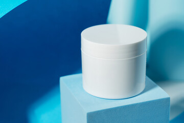 White cosmetic jar on a blue stand on a blue background. Cosmetics, science and medicine. Background for the cosmetics industry.