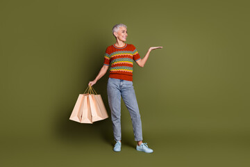 Elderly woman with shopping bags striking a confident pose against a khaki background for fashion and advertising themes