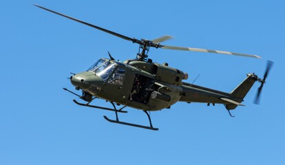 Olive green military helicopter flying in a bright blue cloudless sky.