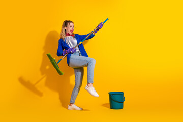 Playful woman posing with broomstick against yellow background showcasing quirky style and energy