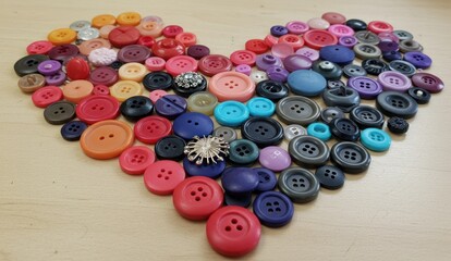 Colorful buttons arranged in a heart shape on a light wood surface.