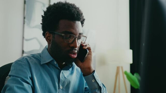 Surprised African American man holding smartphone to ear while reacting to unexpected news. Listening intently and responding with concern during phone call in bright professional office setting.