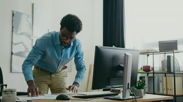 Determined man leaning forward while comparing printed report with on-screen data. Analyzing statistics and verifying information in modern office. Having issues at work. Searching for mistake.