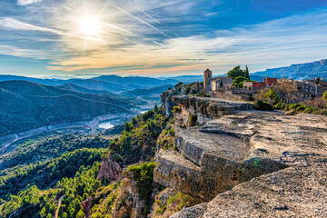 Aerial view of Siurana, Catalonia, with church and mountains. A stunning view of Siurana, Spain, showcasing its church, dramatic cliffs, and sunset.