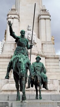 Bronze statues of don quixote and sancho panza at the foot of a stone monument dedicated to miguel de cervantes