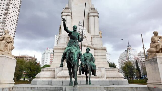 Bronze statues of don quixote and sancho panza at the foot of a stone monument dedicated to miguel de cervantes