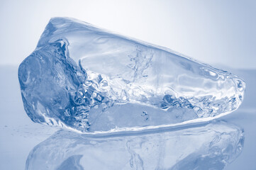 Natural crystal clear ice piece on blue background with reflection