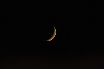 Crescent moon shines brightly in the clear night sky over a tranquil landscape during the early evening hours