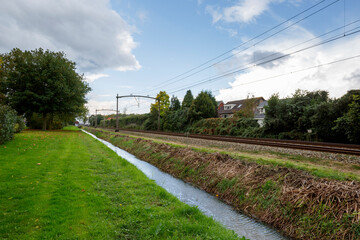 Railway tracks along a grassy embankment with a stream in a rural landscape during daytime
