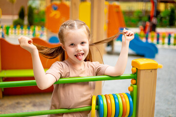 a child girl on the playground in the courtyard of a multi-storey house in the summer has fun...