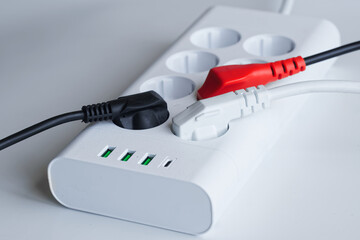 A white power strip with multiple sockets and red/black plugs, showing safe electrical connection. Ideal for tech, energy, or household usage concepts. Photo