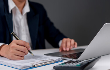 businessman working on papers, taking notes, and analyzing financial data on his laptop.