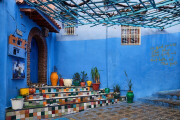 Multicolor steps, orange and yellow flower pots against the blue walls of an empty Tuiles Colorees in the old town medina, Chefchaouen, Morocco