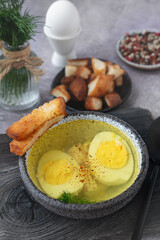 A bowl of homemade chicken broth with eggs and crusty bread served on a rustic wooden board