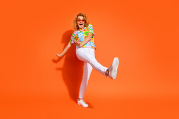 Vibrant young woman posing playfully against a radiant orange background, showcasing her casual and...